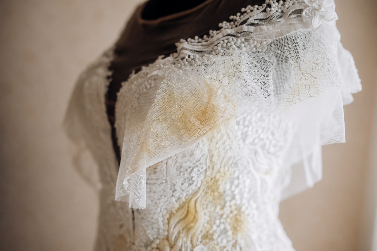 A close-up of a white lace wedding dress with visible yellowish stains on the fabric and neckline.